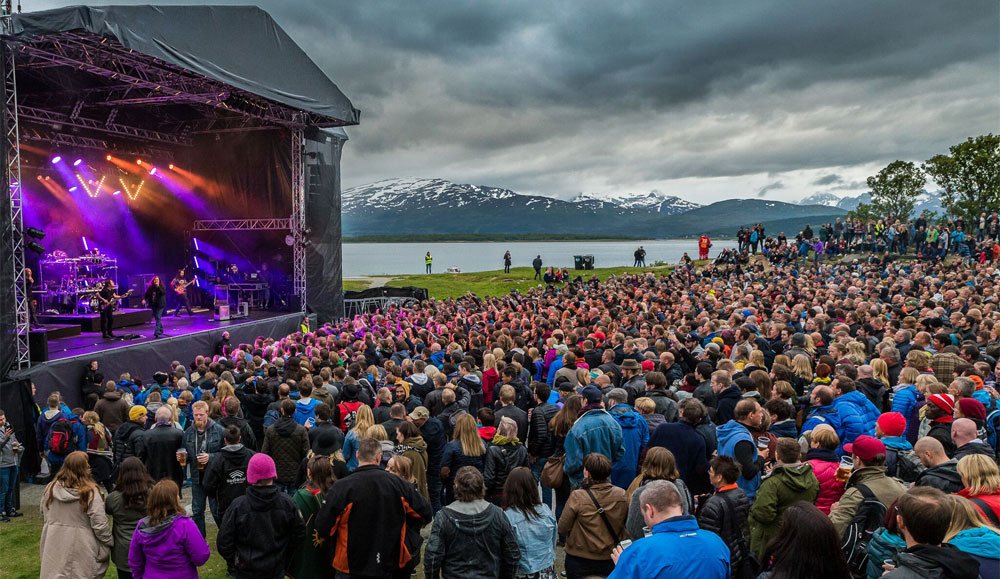 Publikum foran scenen på Bukta, med fjell og fjord i bakgrunnen